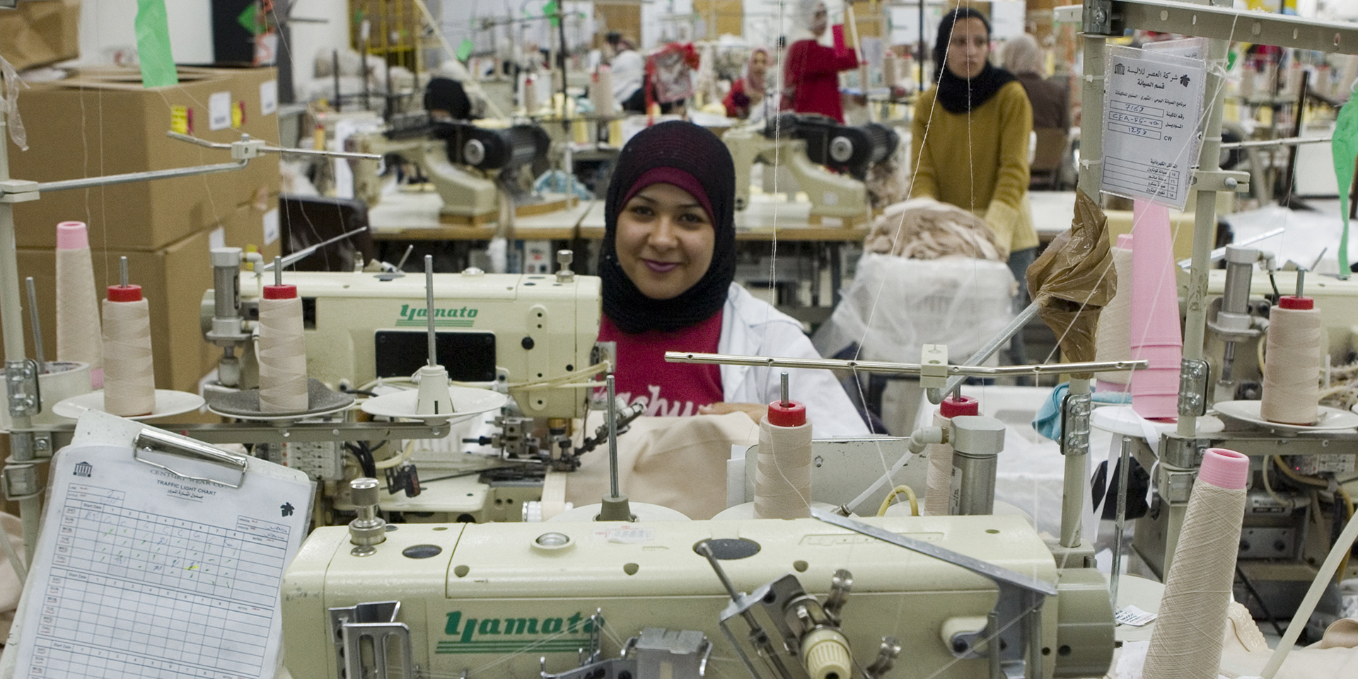 A woman smiles from behind a sewing machine at Century Wear Factory in Irbid, Jordan
