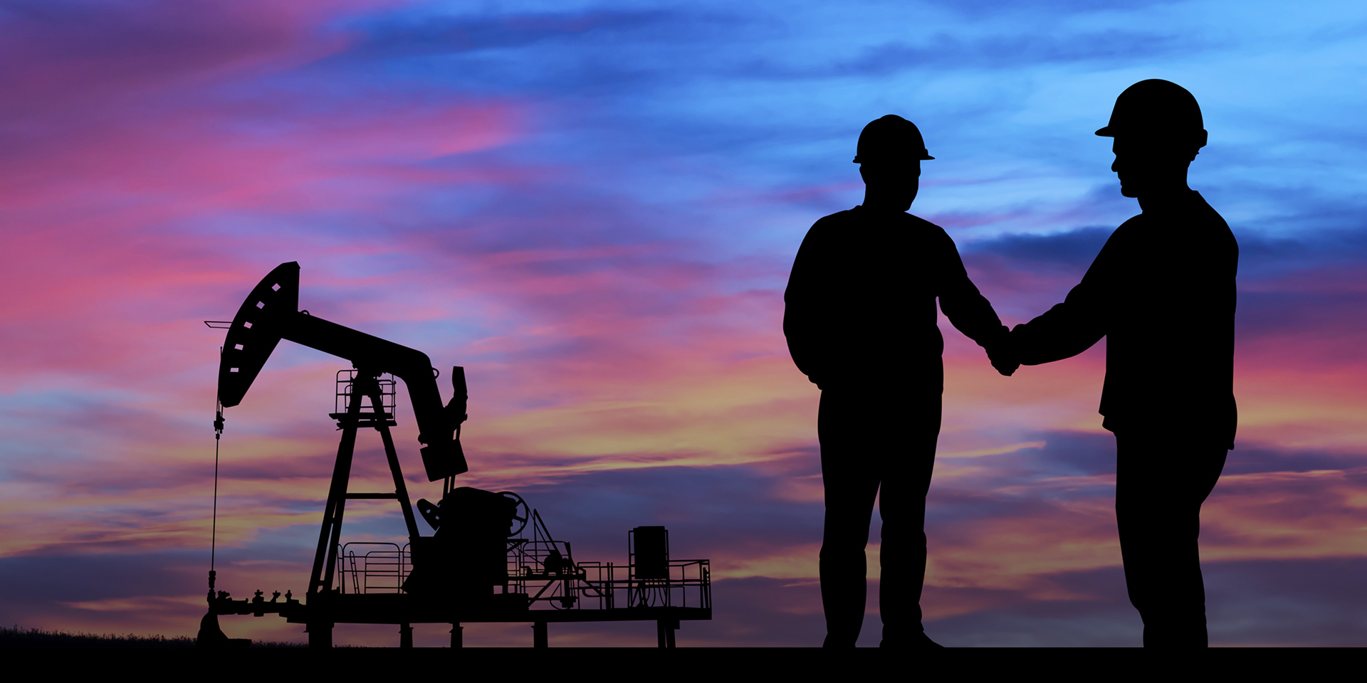 Two people shake hands in front of equipment at an oil field.
