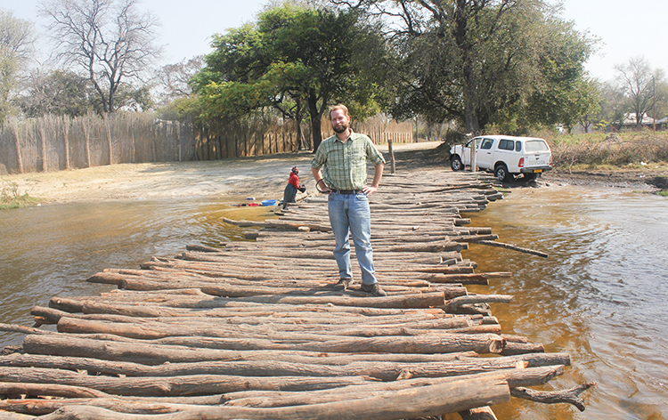 Brian App standing on a river crossing comprised of logs