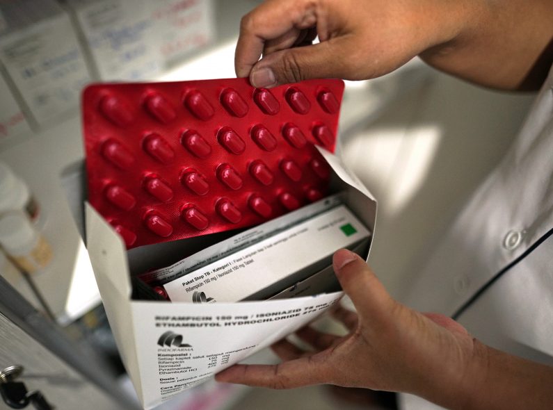 A pharmacist is holding a package of pills for tuberculosis treatment.