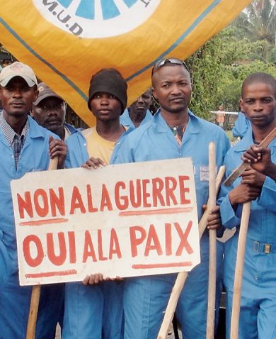 Congolese men dressed in blue stand holding a sign asking for peace