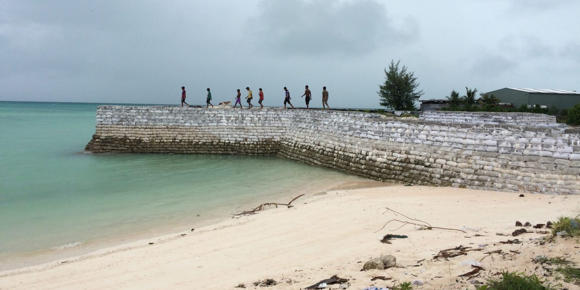 A group of young people walk along a sea wall in Tarawa, Kiribati.
