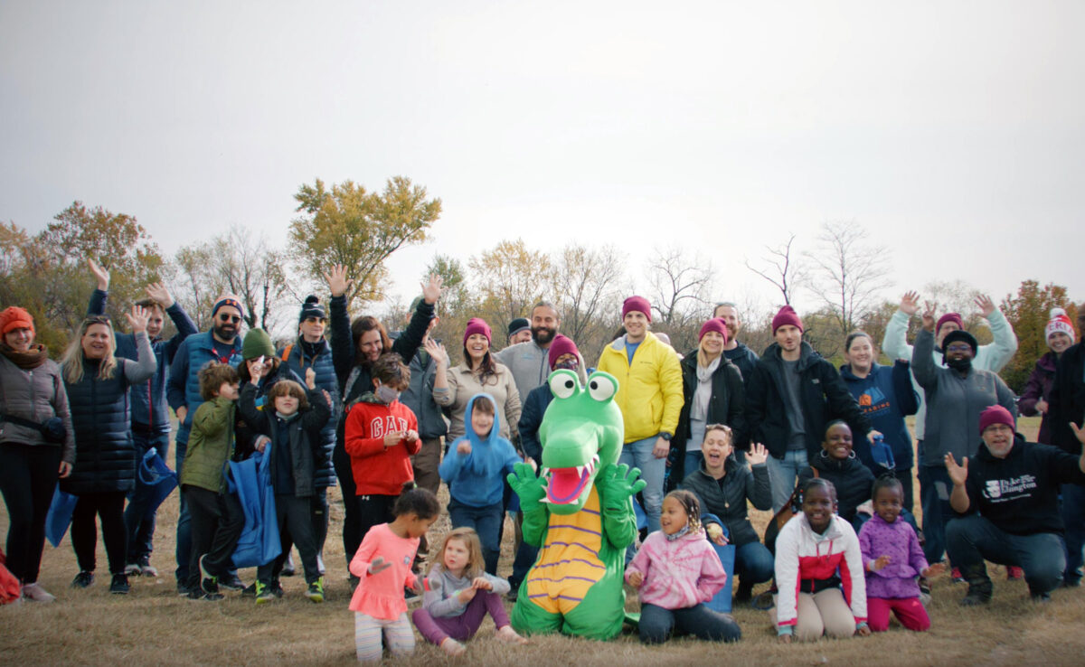 Participants of the clean-up event wave to the camera on the banks of the Anacostia River