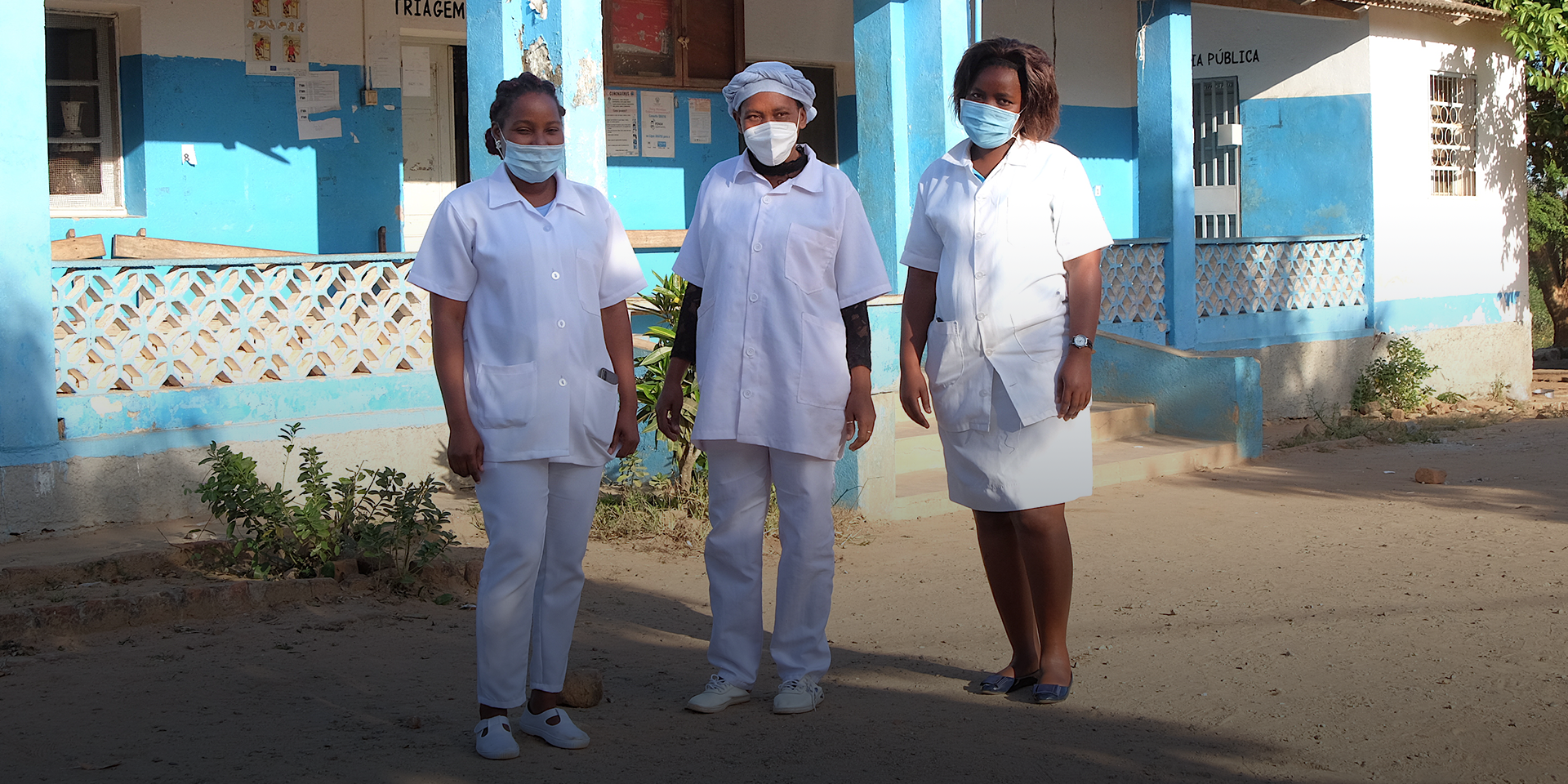 Three midwives stand outside a healthcare clinic in Mozambique.