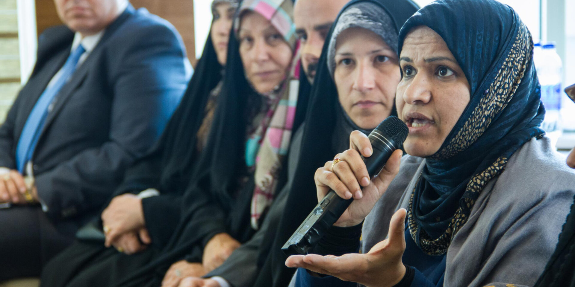 An Iraqi woman wearing a headscarf speaks into a microphone at a meeting.