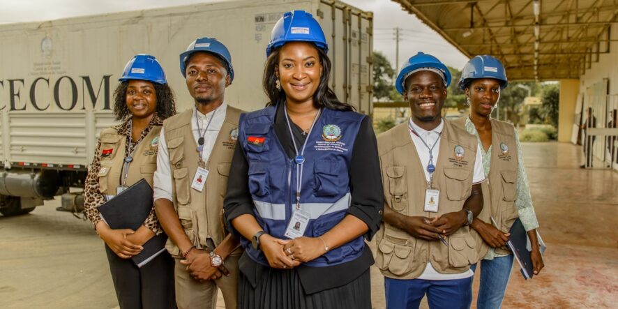 Four people wearing blue hard hats and vests look straight at the camera