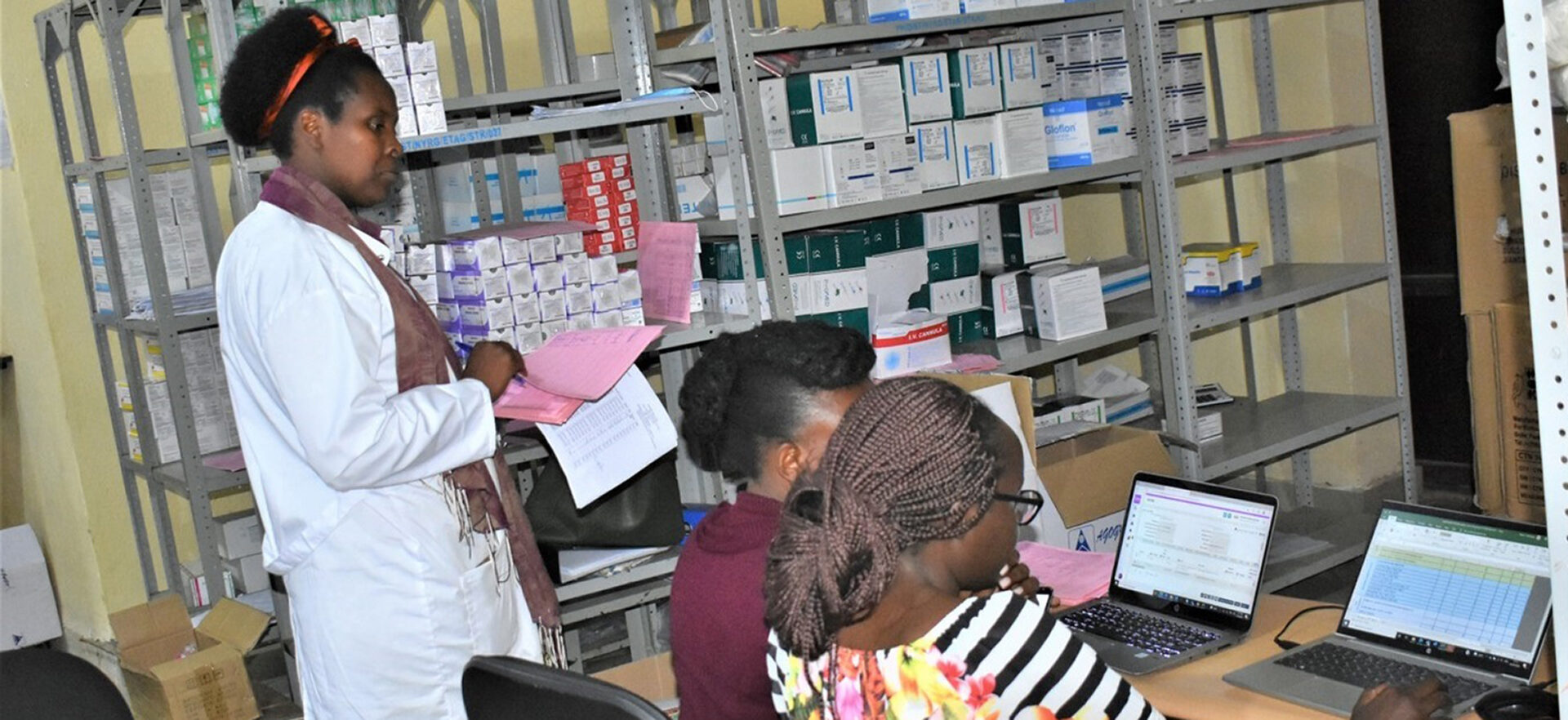Two women look at a computer, one woman stands next to them holding a clipboard