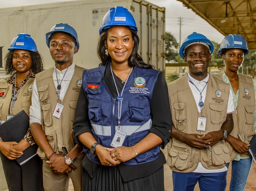 Four people wearing blue hard hats and vests look straight at the camera
