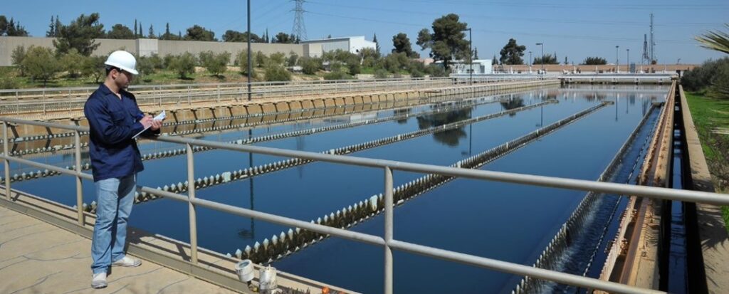 A person with a clipboard stands next to a water treatment facility
