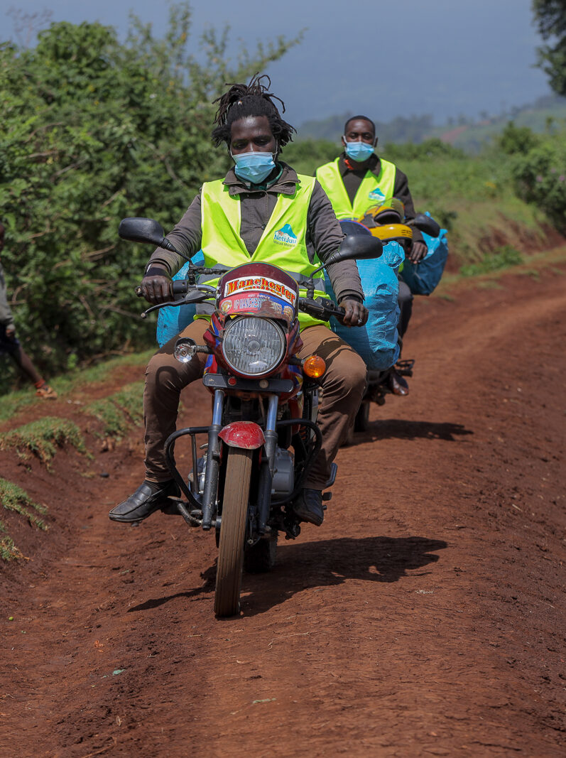 Two men on motorcycles transport malaria nets on a dirt road