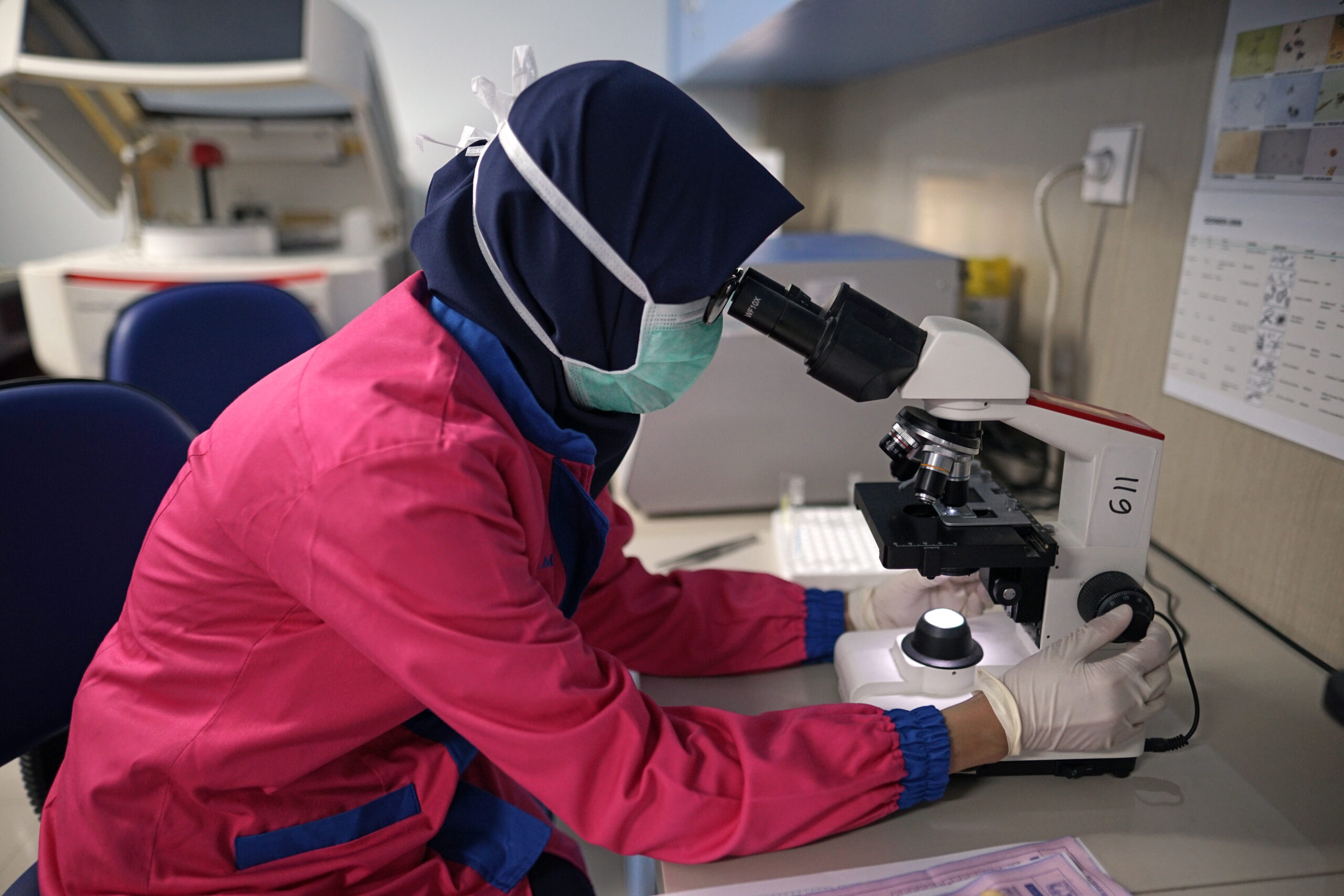 A woman in a lab peers through a microscope