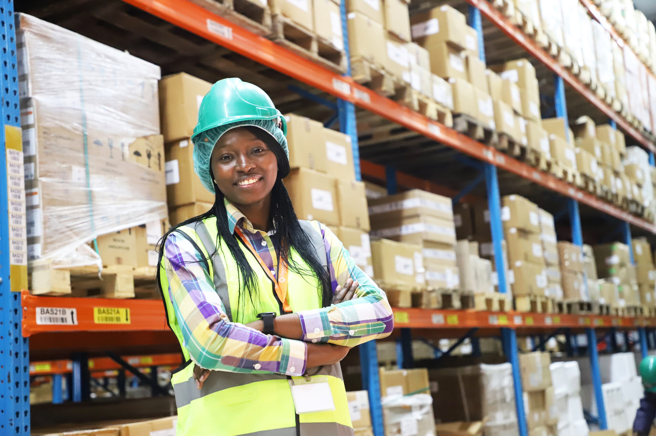 A smiling woman wearing safety gear in the middle of a warehouse