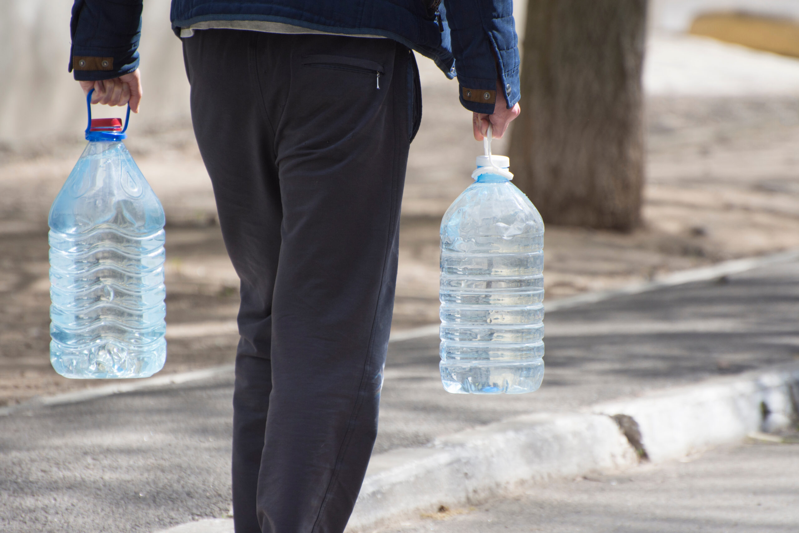 Man carries two large bottles of water.
