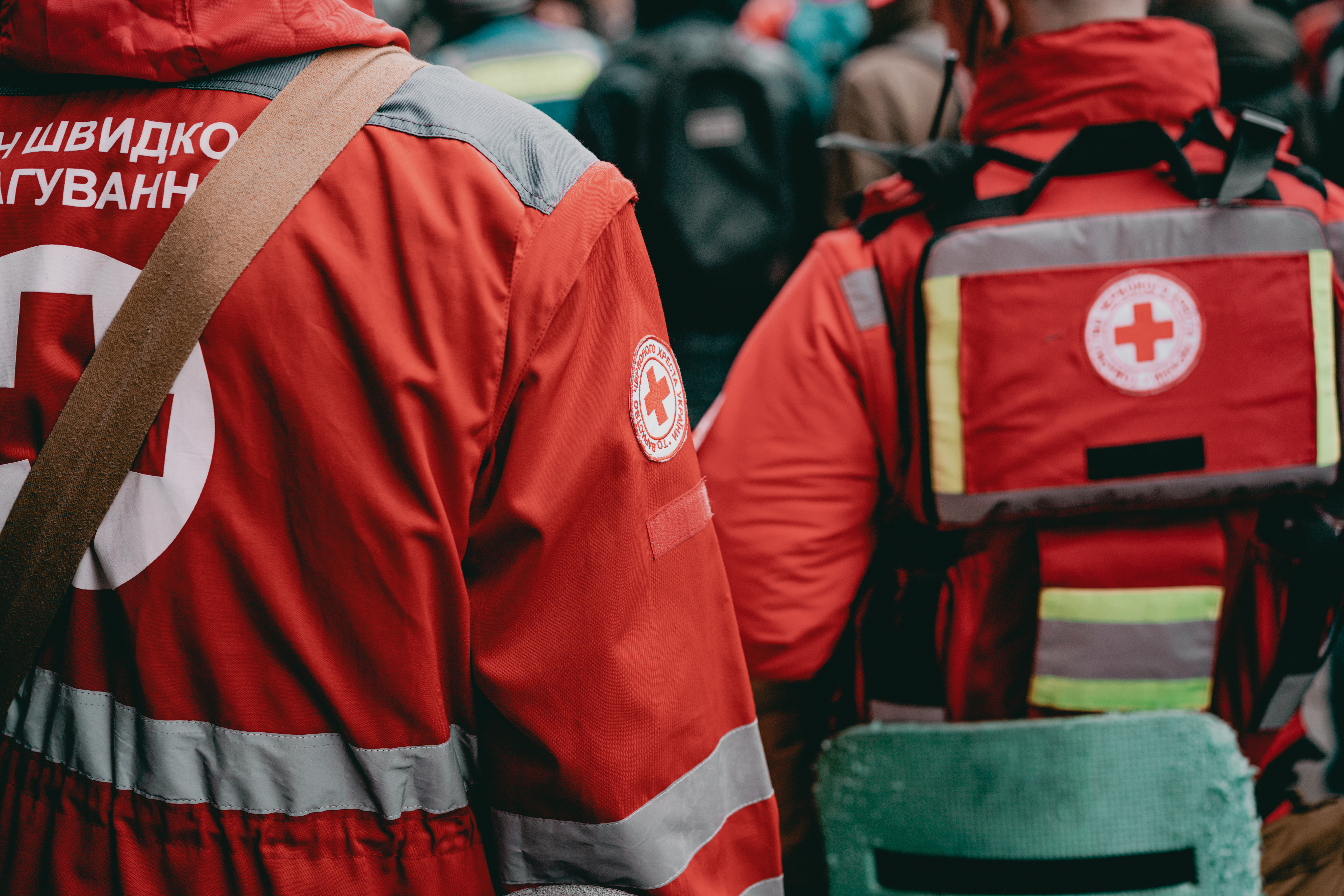 A crowd of emergency medic assistants in red uniforms with backpacks stand outdoor on the street.