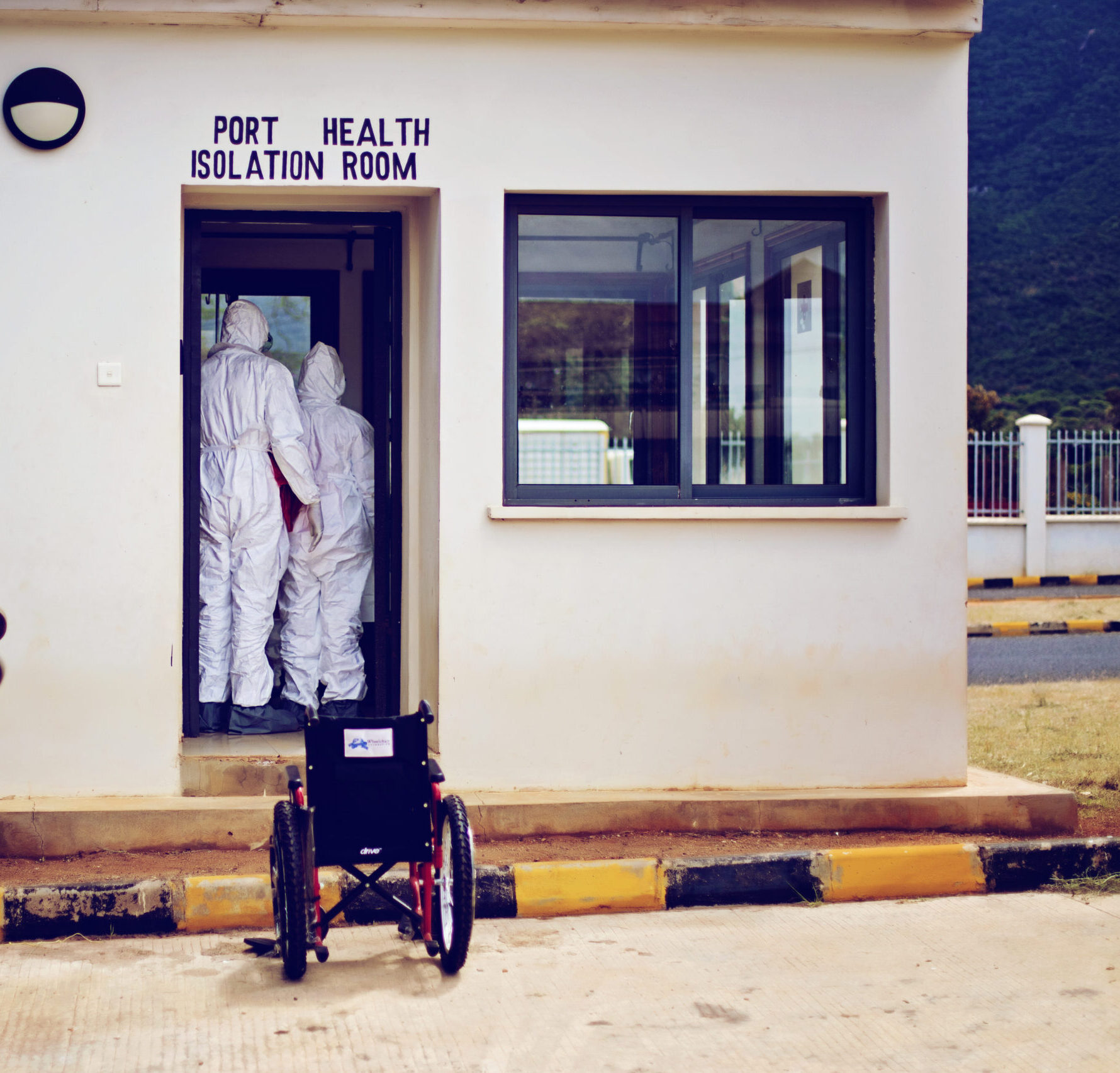 Two health workers in full PPE stand in the doorway of a building