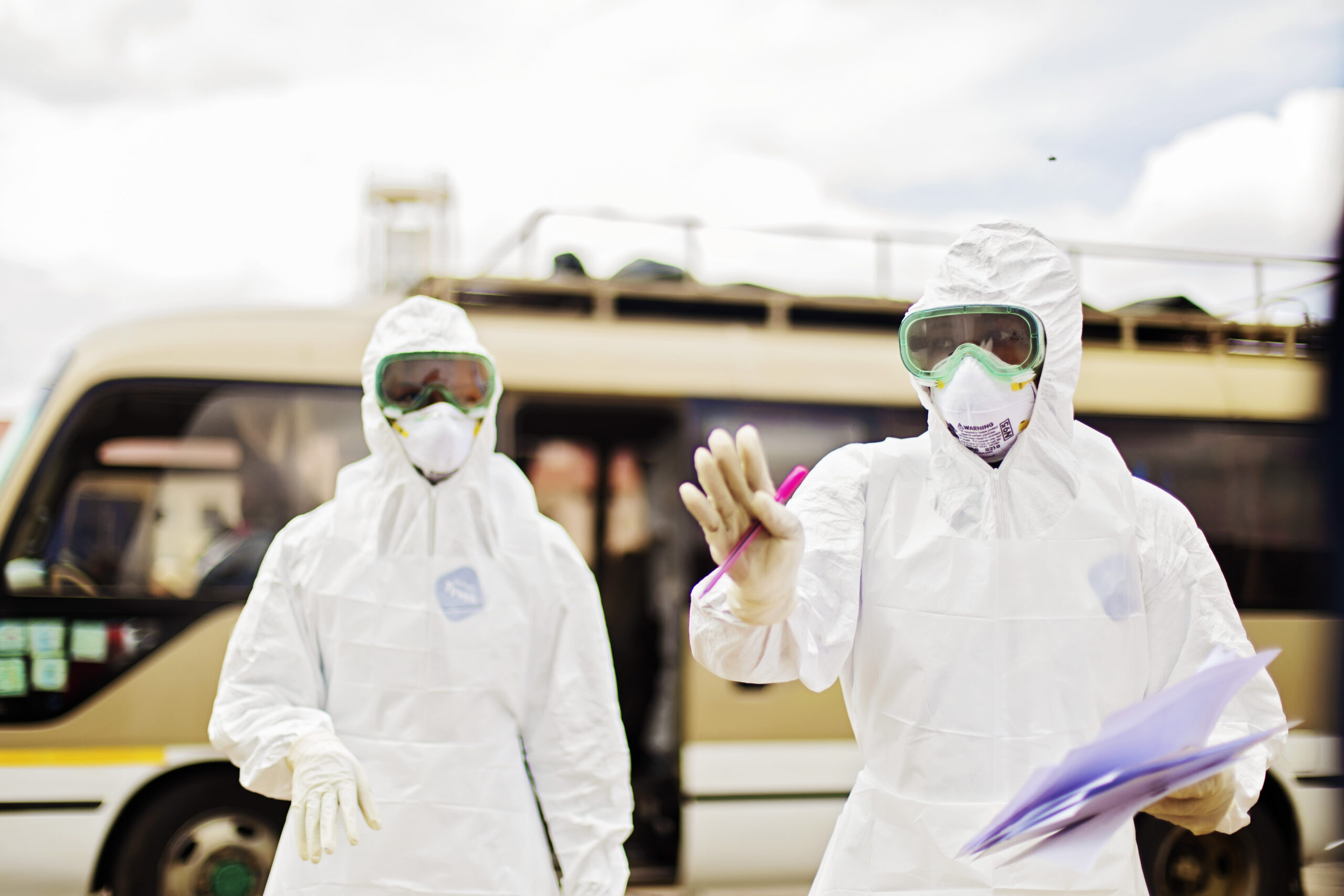 Two people in full PPE hold papers and face the camera